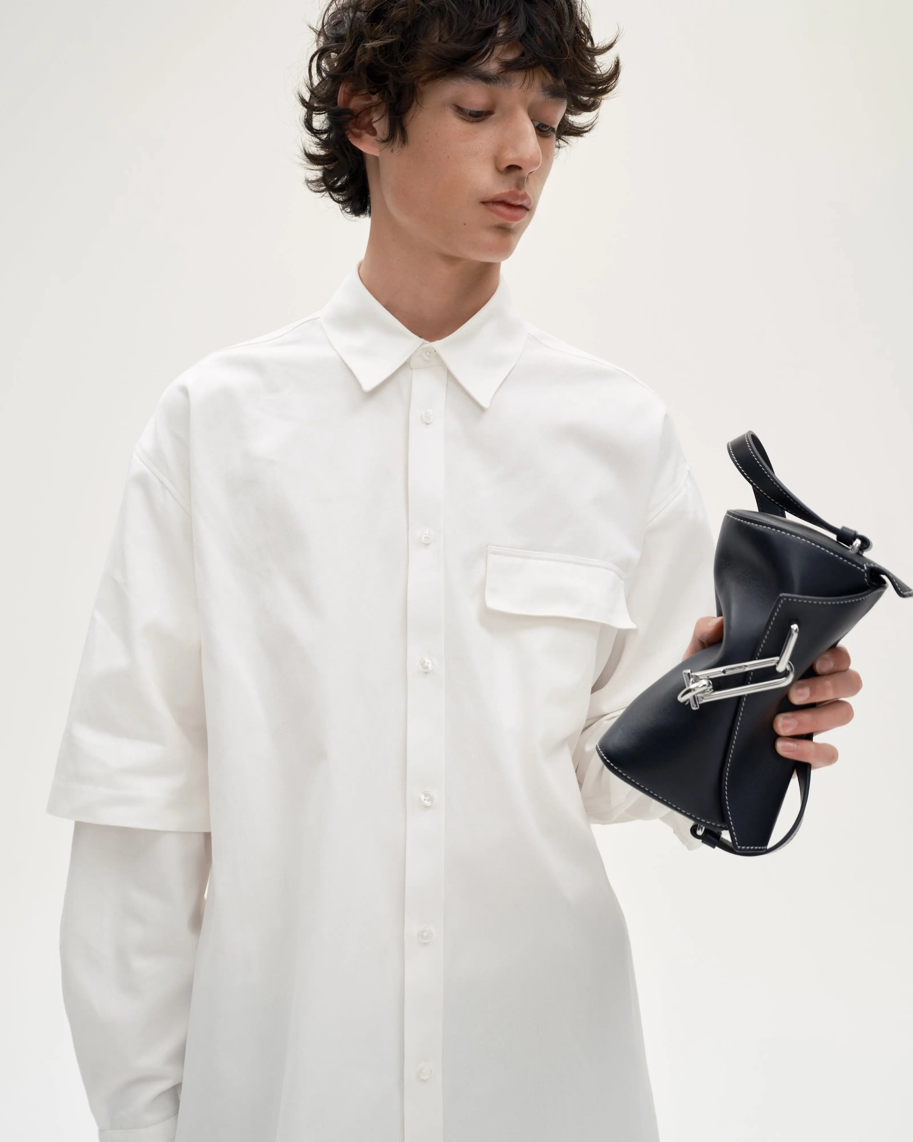 Model-holding-TAD-FAB-Softie-Mini-matte-black-calfskin-shoulder- bag-with-silver-tone-carabiner-style-buckle